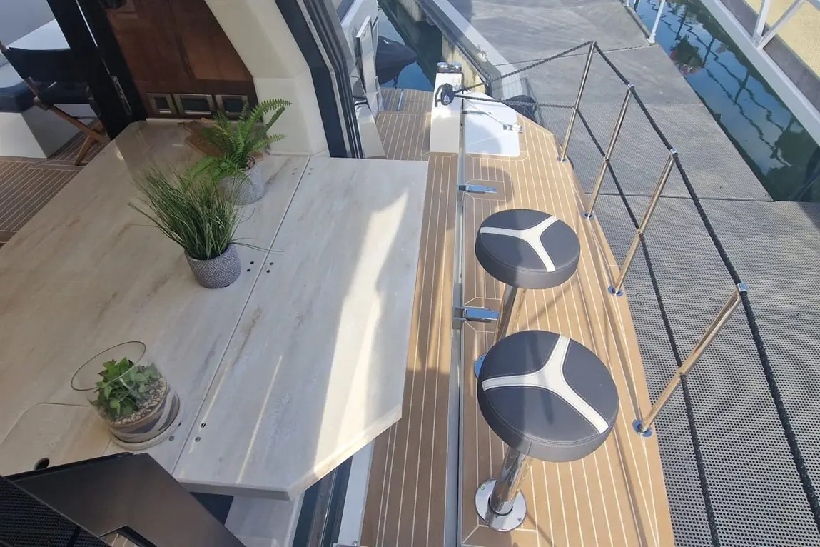 Stylish outdoor seating area on a boat, featuring two black and white bar stools, a table, and decorative plants.